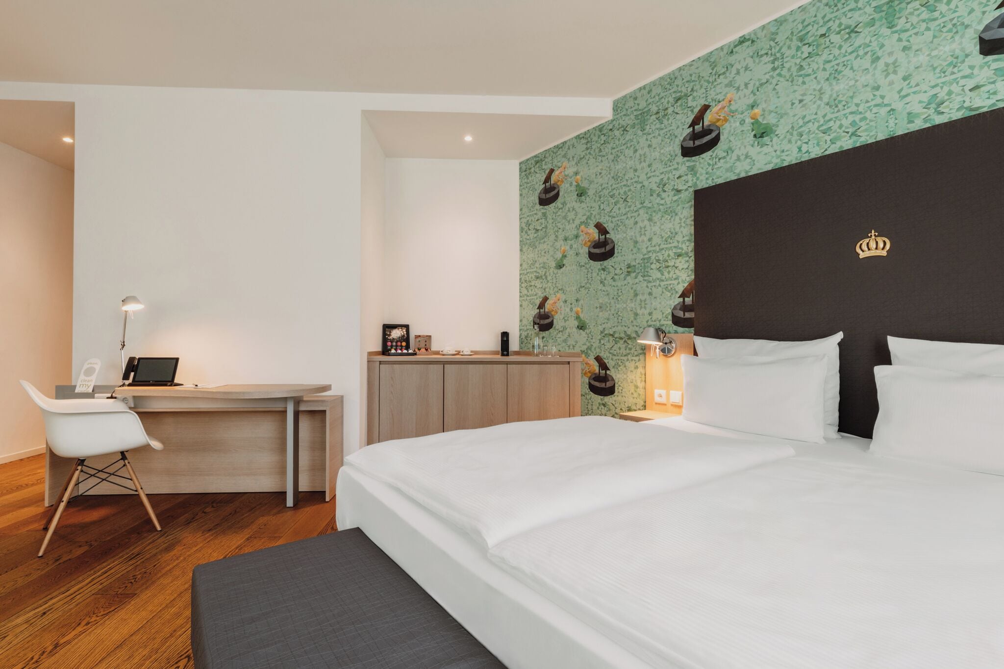 A hotel room with a bed, desk, chair, and a wall with a pattern.