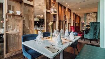Ein Restaurant mit modernem Interieur, das einen langen Esstisch, blau gepolsterte Stühle und eine Theke im Hintergrund zeigt.