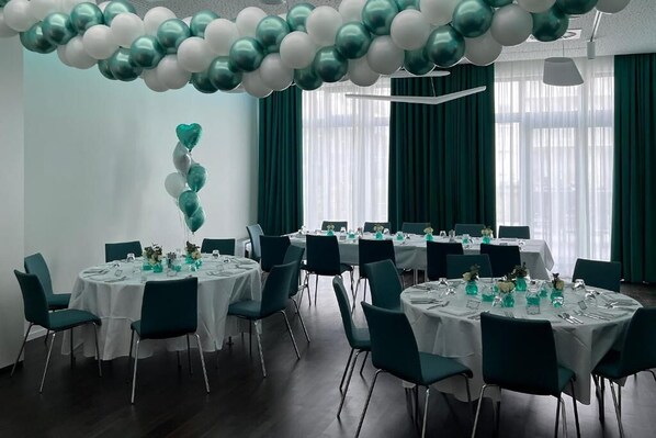 Une salle de conférence avec des tables rondes, des chaises de couleur turquoise et des nappes blanches.
