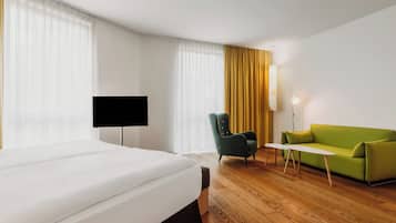 Habitación de hotel con cama, sofá verde, silla, televisor y lámpara.