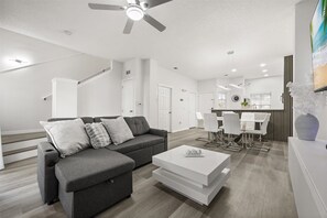 A modern living room with a grey sectional sofa, white coffee table, and a dining area with white chairs and a black and white striped wall. - Last Chance For A Labor Day Escape/ 5th Night Free! (Kissimmee)