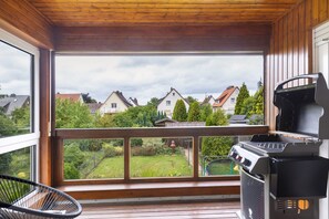 Un balcón con vistas a casas, una parrilla y una silla.