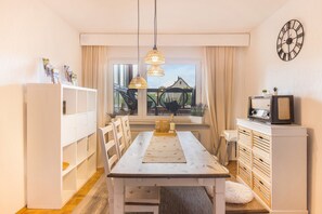 A dining area with a wooden table, white chairs, pendant lights, and a view of the outdoors. - Apartment Gartenblick – Spacious Retreat with Garden View in Korbach (Korbach)