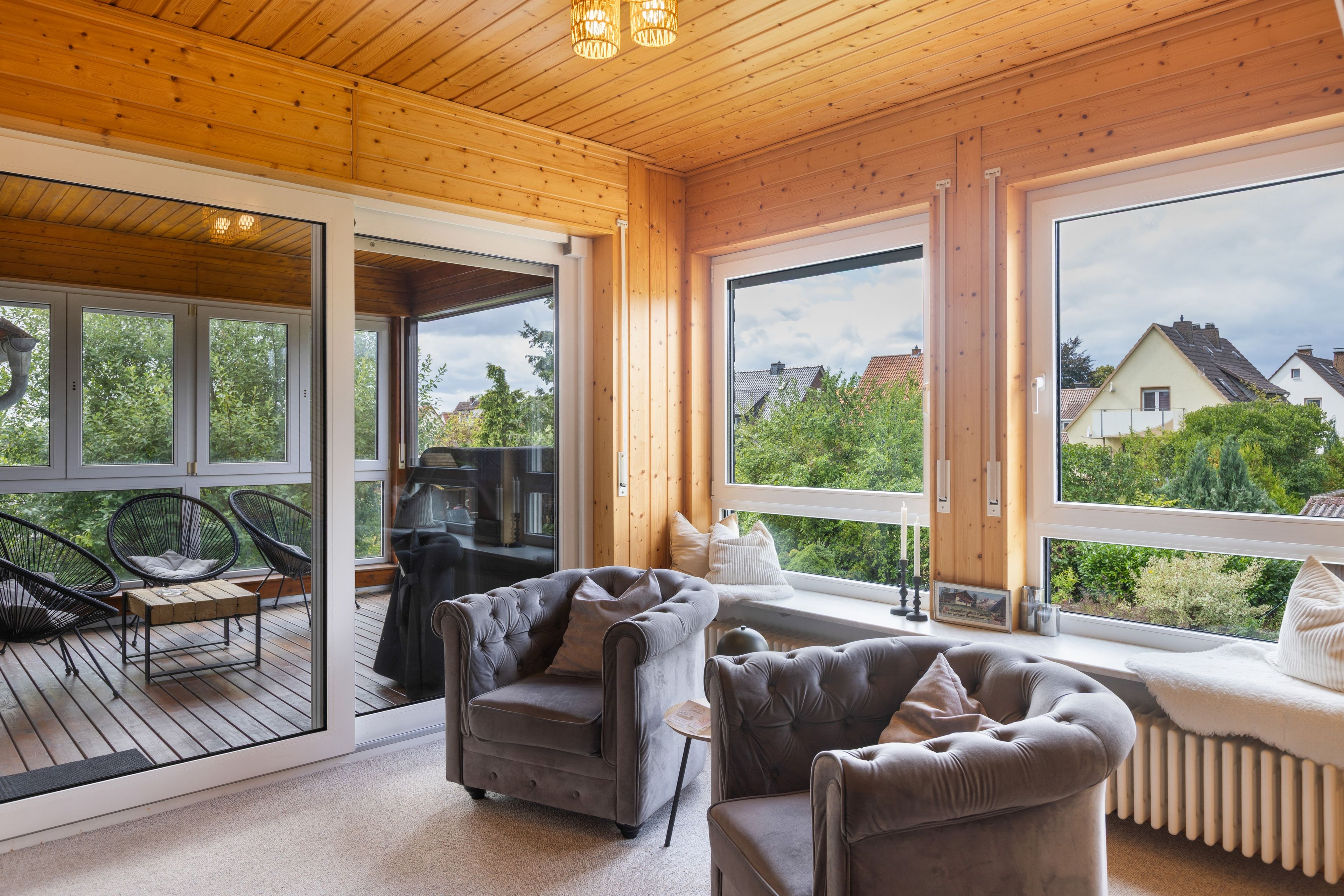Una habitación acogedora con techo de madera, ventanas amplias y una zona de estar cómoda con dos sofás y una silla.