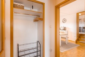 Un pasillo con un marco de puerta de madera, un perchero metálico y una pared blanca con un reloj.