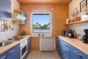 Cocina compacta con vistas a casas a través de una ventana, una tetera, una cafetera y un radiador.