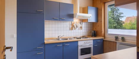 Una cocina moderna con armarios azules, una estufa blanca y una ventana con vistas a zonas verdes.