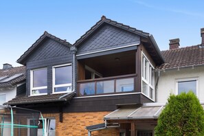 Une maison à deux étages dotée d’un balcon, de grandes fenêtres et d’une façade en briques.
