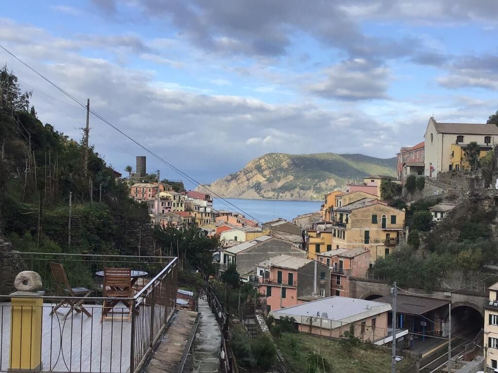 Ein Küstendorf mit bunten Häusern, einem gepflasterten Weg und Blick auf das Meer und die Hügel.