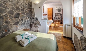 A room with a stone wall, a bed with towels, a wooden door, and a view through an archway. - Camere Giuliano Basso (Vernazza)