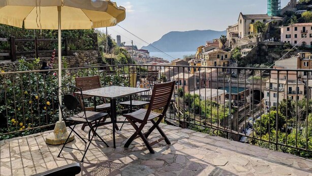 Une terrasse avec une table et des chaises, un parasol jaune et une vue sur une ville située sur une colline.