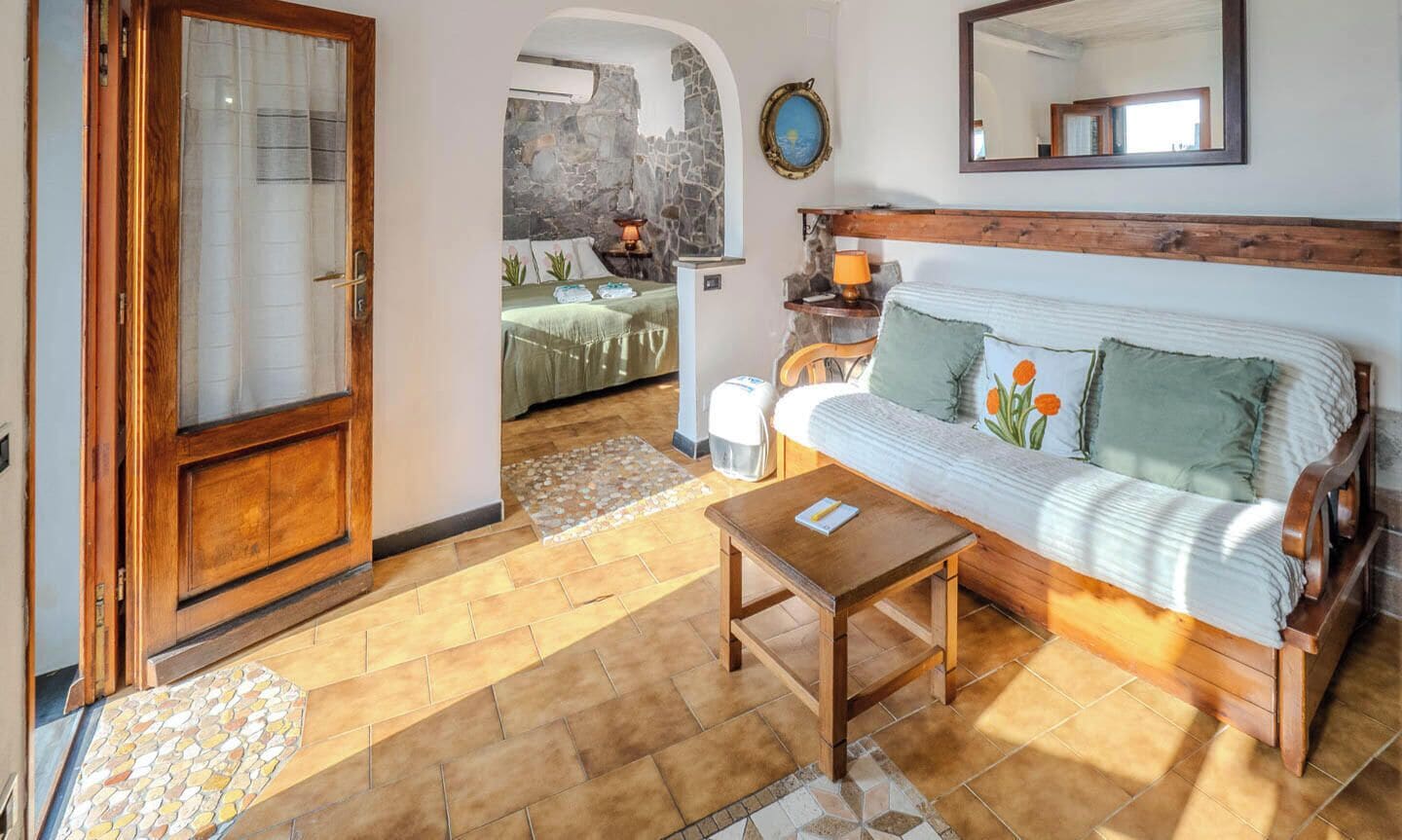 Una habitación acogedora con puerta de madera, un sofá con cojines, una mesita y una pared de piedra.