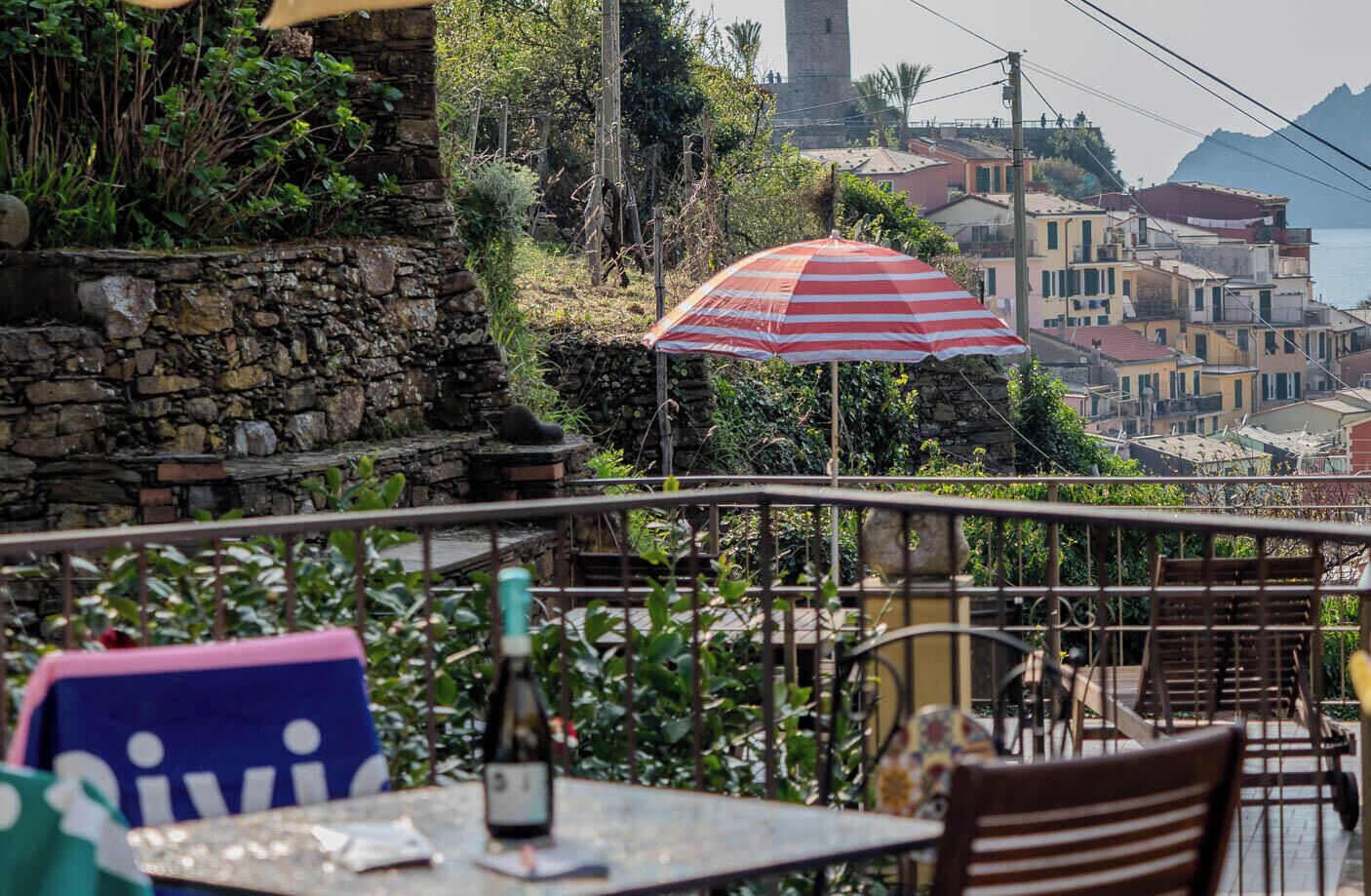 Une terrasse avec un mur en pierre, une table avec une bouteille et un parasol à rayures.