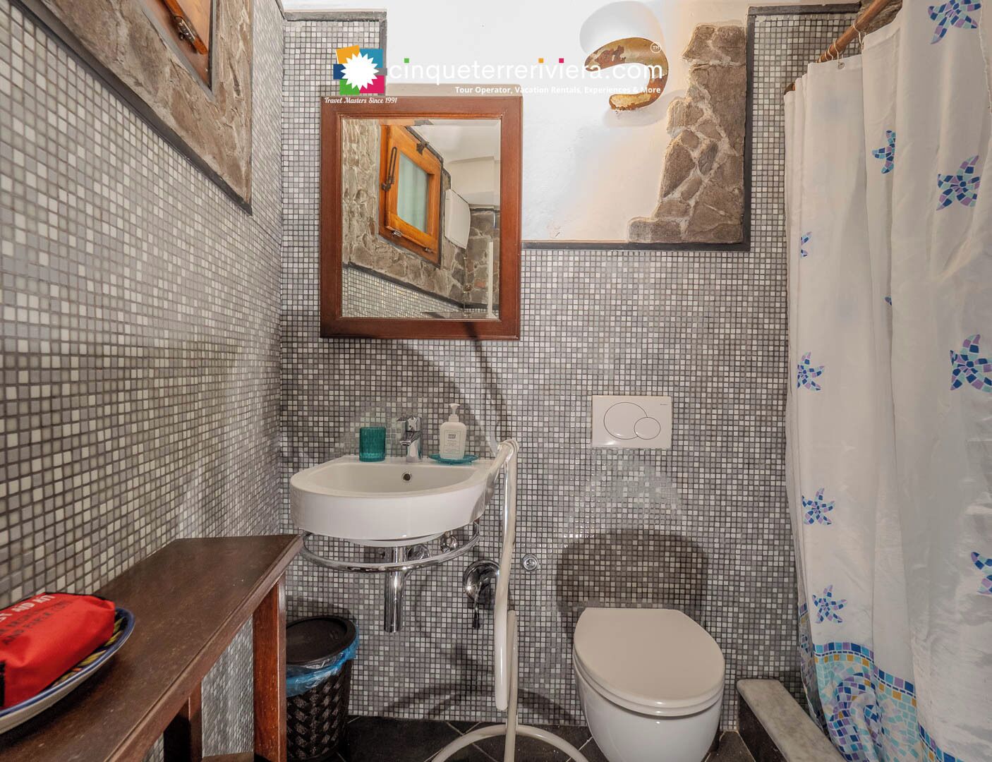 Um banheiro com parede revestida de azulejos, pia, espelho, vaso sanitário e cortina de chuveiro.