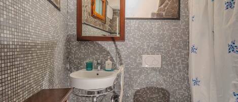 Um banheiro com parede revestida de azulejos, pia, espelho, vaso sanitário e cortina de chuveiro.
