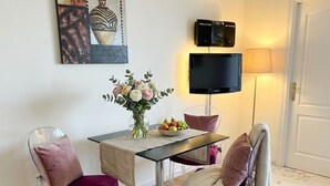 Een eethoek met een tafel, stoelen, een bloevas, een fruitschaal, een flatscreen televisie en een lamp.