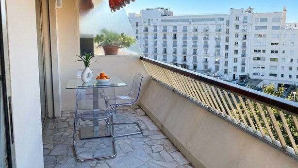Een balkon met vrij uitzicht op een stadsbeeld, een bloempot, een tafel met stoelen en een rode luifel.