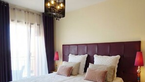 Een hotelkamer met een groot bed, twee bedlampen, een kroonluchter en uitzicht op het omliggende landschap.