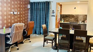 A room with a dining table, chairs, a ceiling fan, a shower area, and patterned wallpaper. - Stay Royal Landran (Sahibzada Ajit Singh Nagar)
