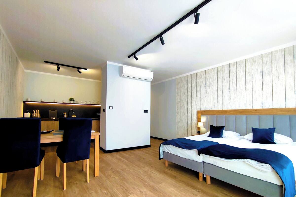 A modern hotel room with a wooden floor, a desk with a chair, a bed with two pillows, and a wall-mounted air conditioner.