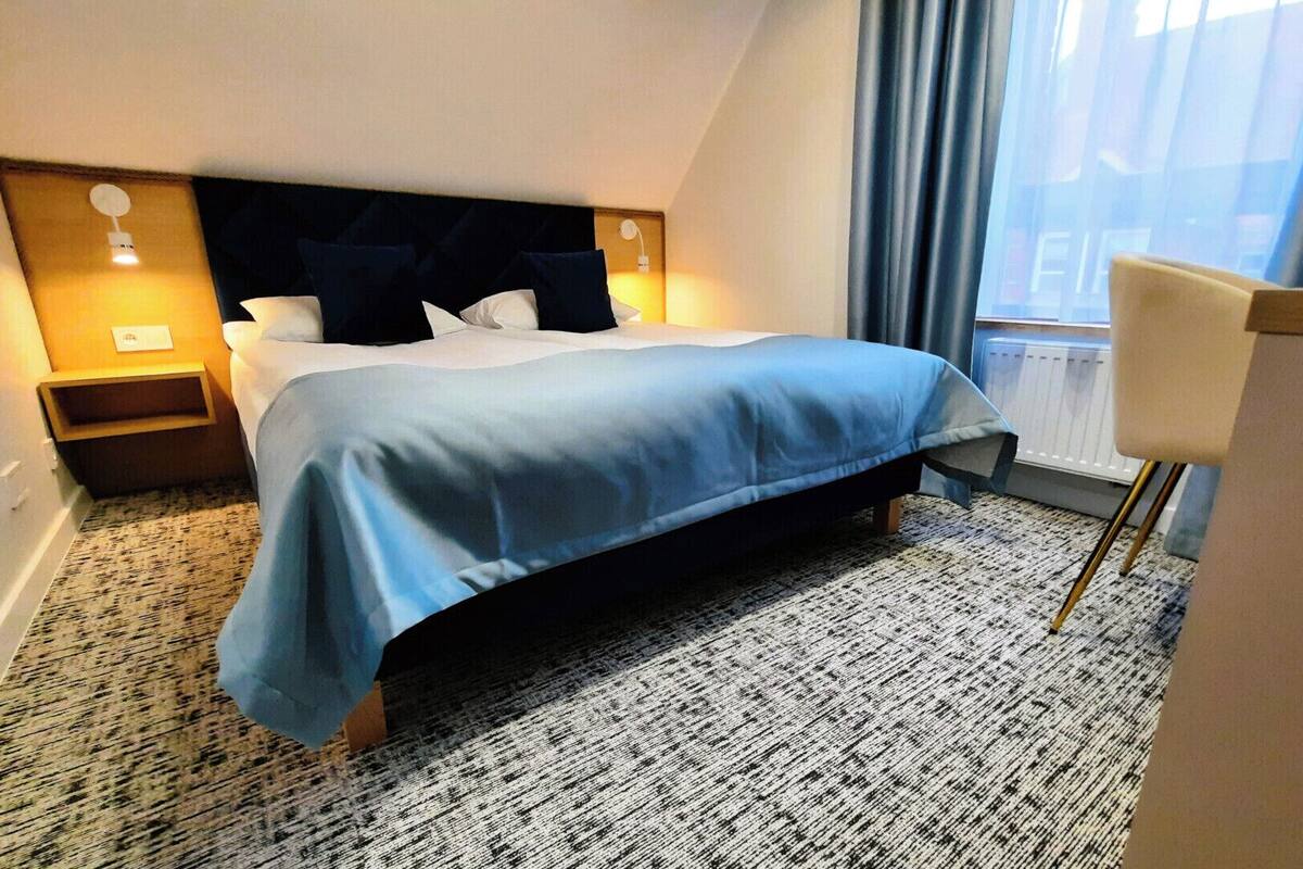 A hotel room with a bed, a nightstand, a chair, and a window with curtains.