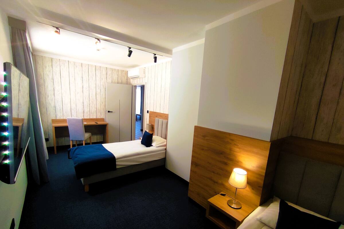 A hotel room with a bed, bedside table, lamp, desk, chair, and a wardrobe.