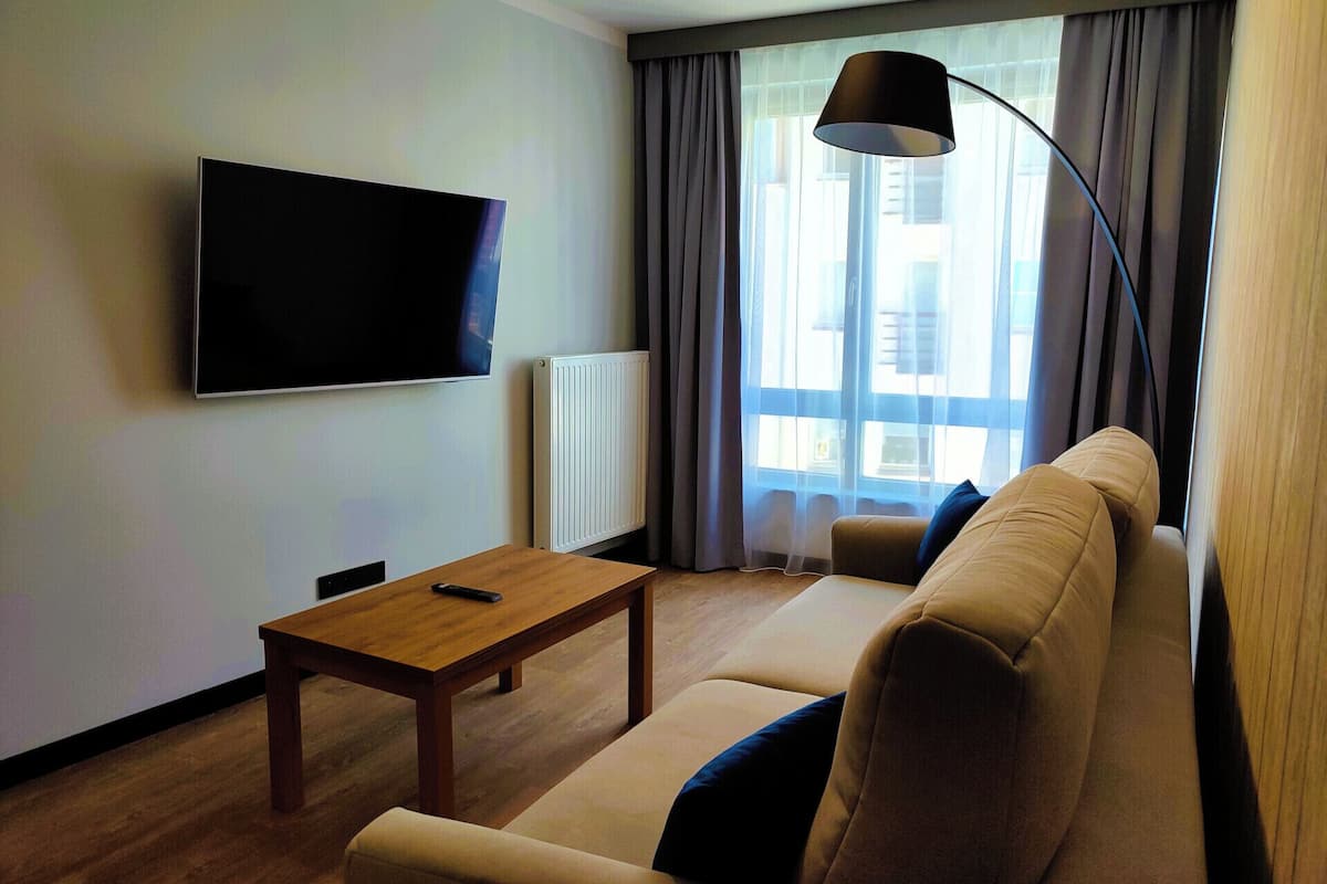 A modern living room with a flat-screen TV, a wooden coffee table, a beige sofa, and a floor lamp.