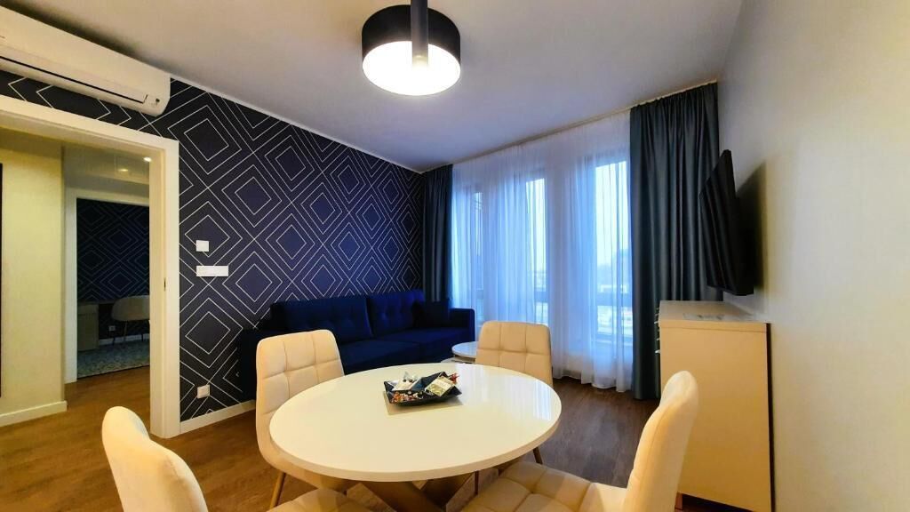 Une chambre d’hôtel moderne avec une table de salle à manger ronde, un canapé bleu et un téléviseur à écran plat.