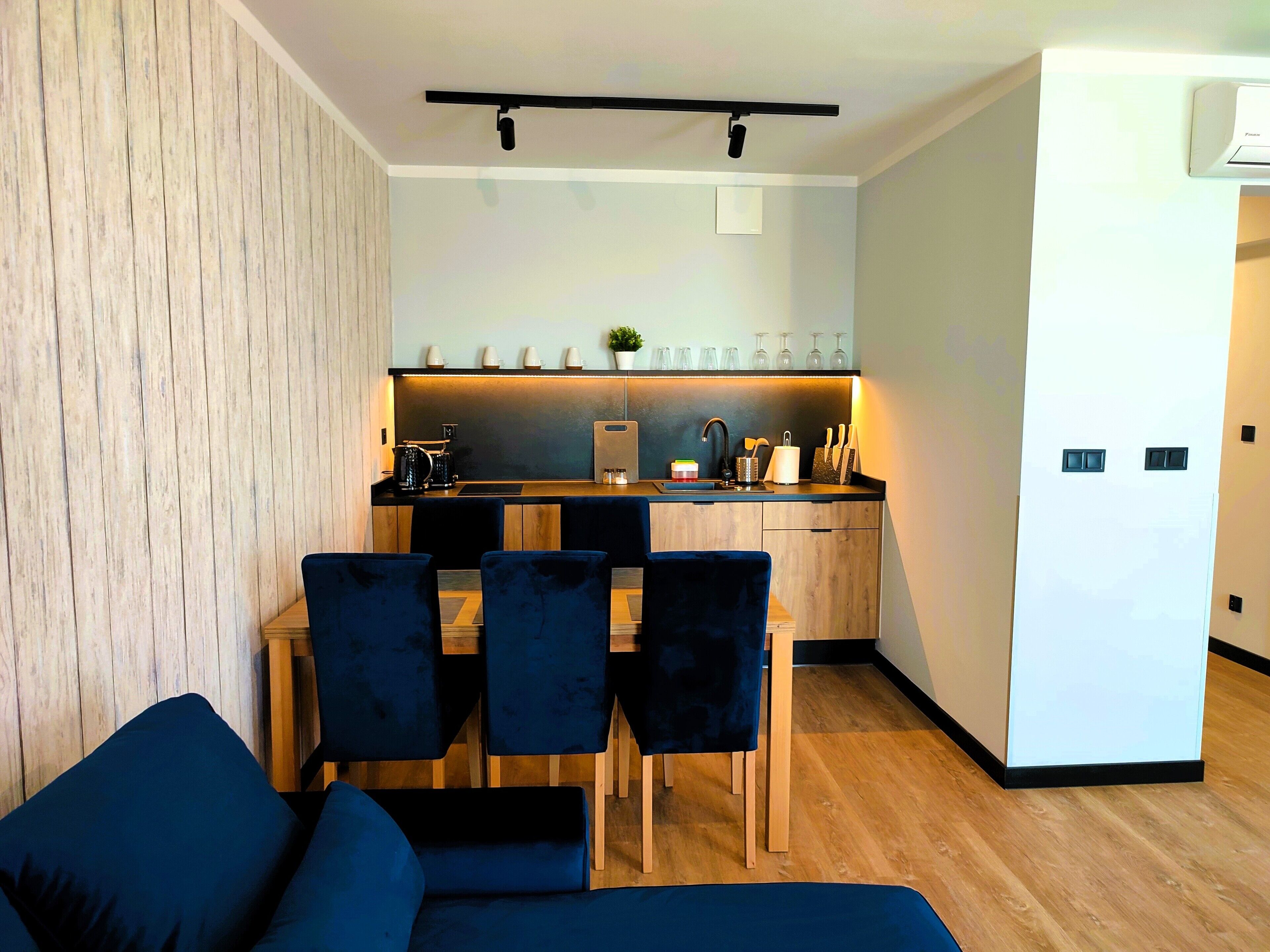 Een compacte woonruimte met een kitchenette, een eethoek met tafel en stoelen, en een bank.