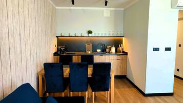 Een compacte woonruimte met een kitchenette, een eethoek met tafel en stoelen, en een bank.
