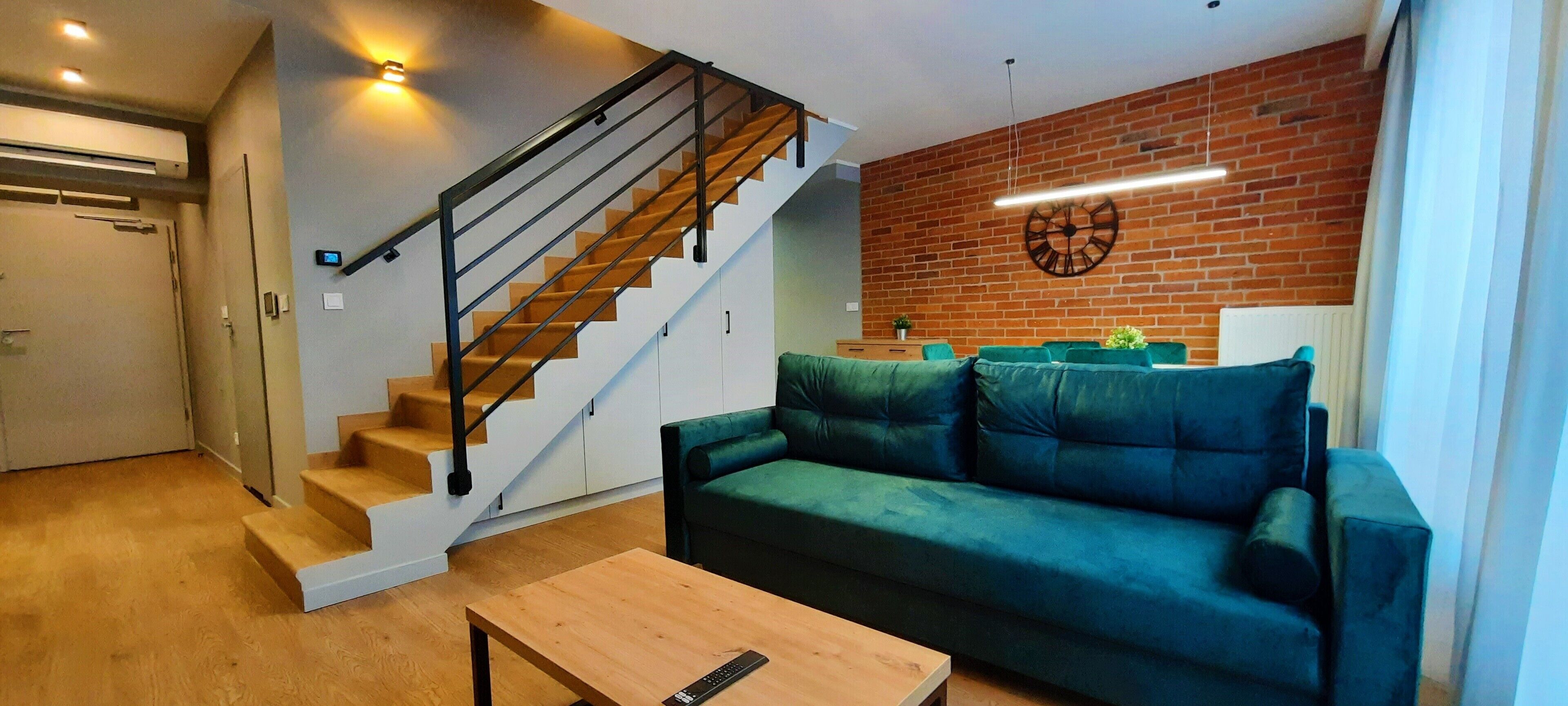 A modern living room with a wooden staircase, a green sofa, and a wooden coffee table.
