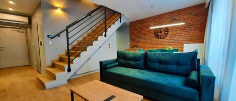 A modern living room with a wooden staircase, a green sofa, and a wooden coffee table.
