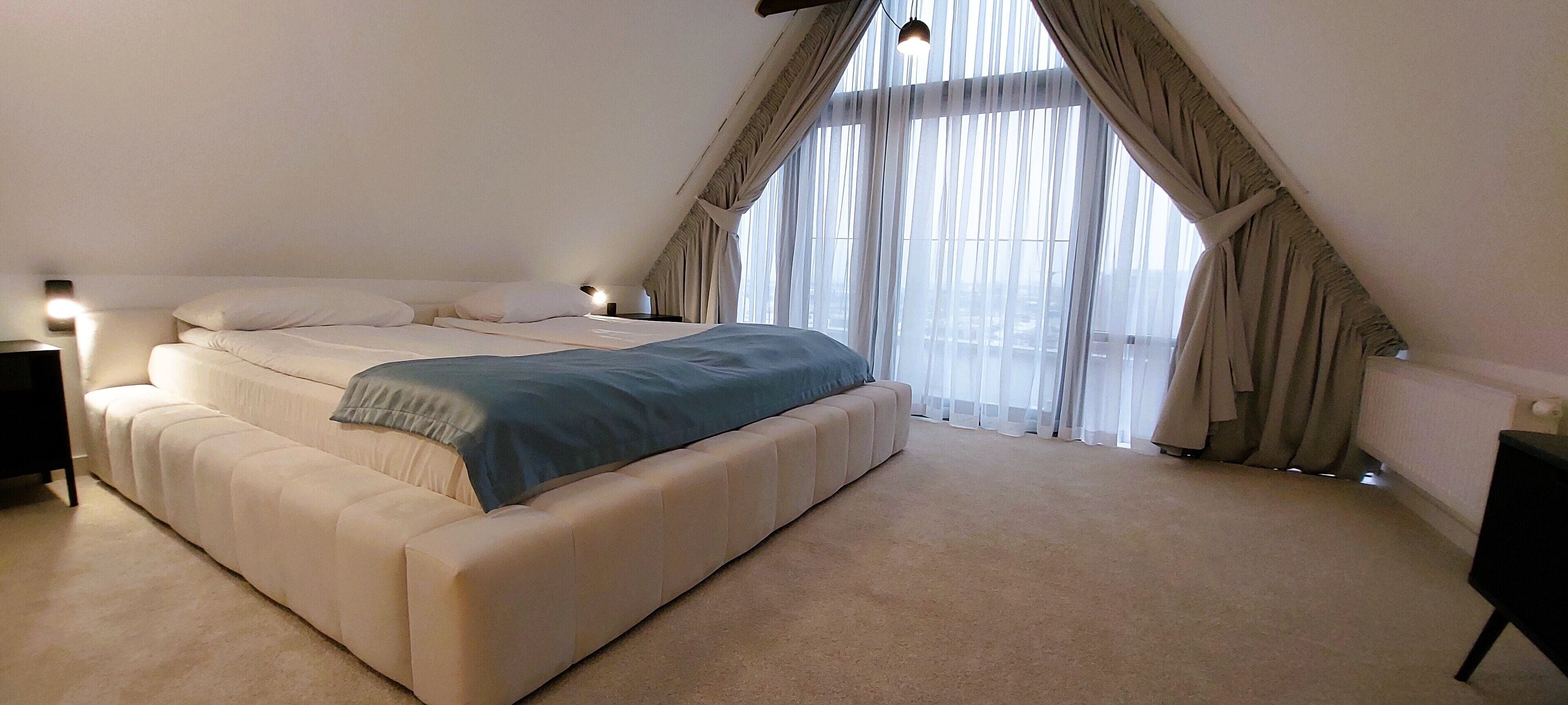 Un dormitorio con una cama grande, una mesita de noche y una ventana con cortinas.