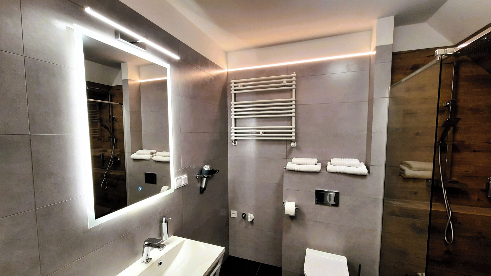 A modern bathroom with a large mirror, a white sink, a towel rack, and a shower.