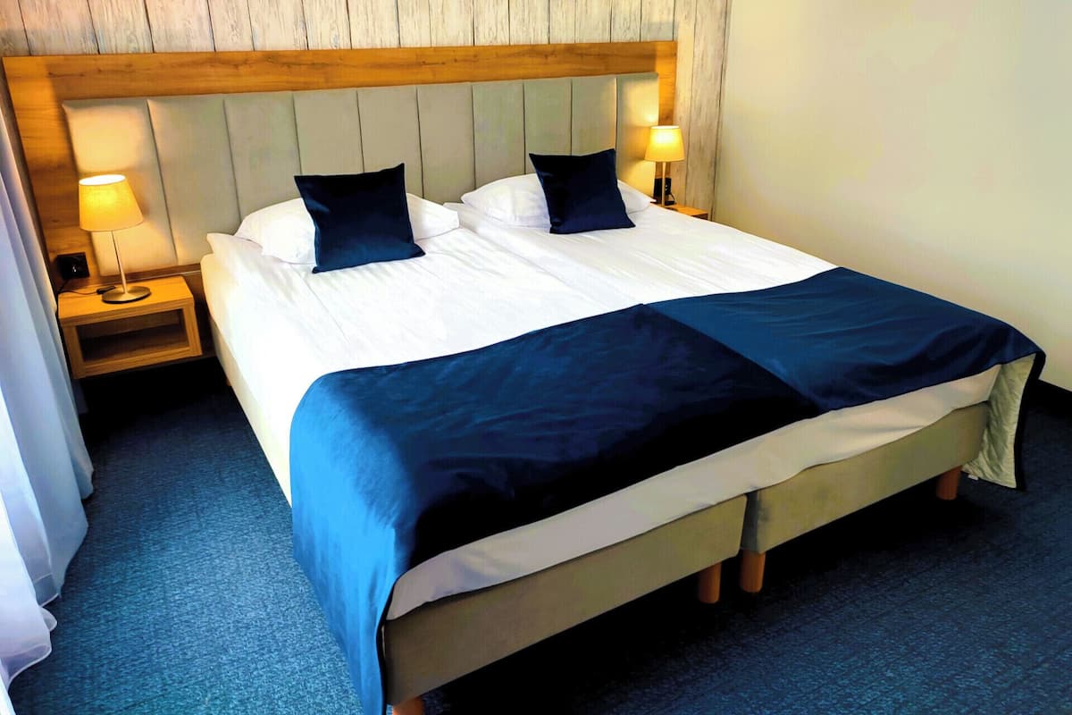 A neatly made bed with a wooden headboard, two bedside lamps, and a blue carpet.