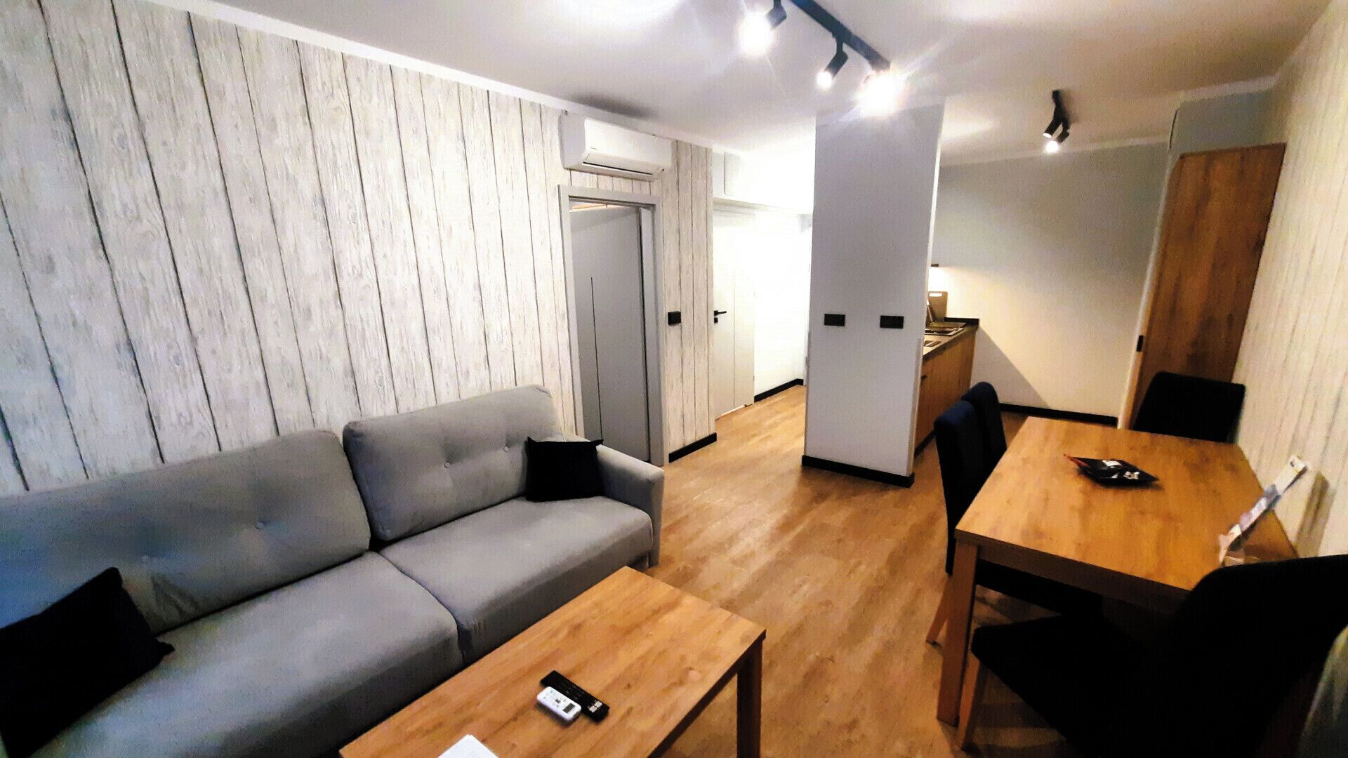 A modern living room with a grey sofa, a wooden coffee table, and a dining area with a wooden table and chairs.