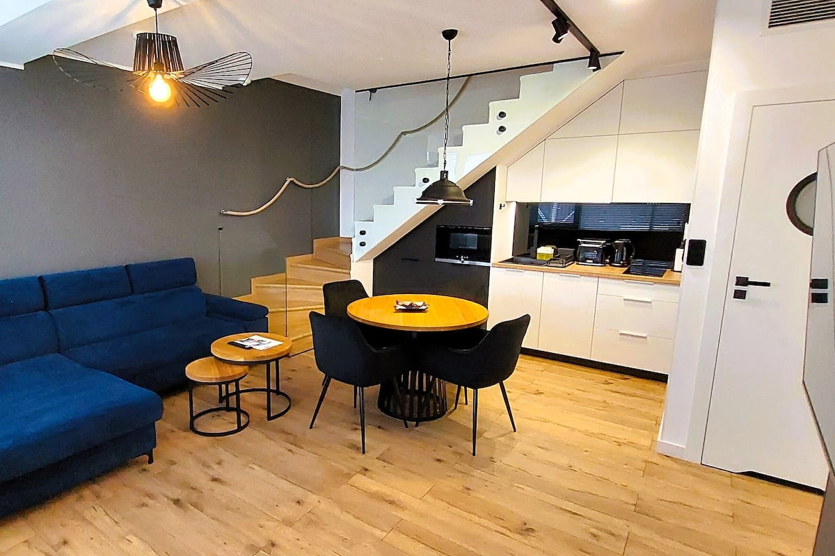 A modern living space with a blue sofa, a small round table, and a staircase leading to a kitchen.