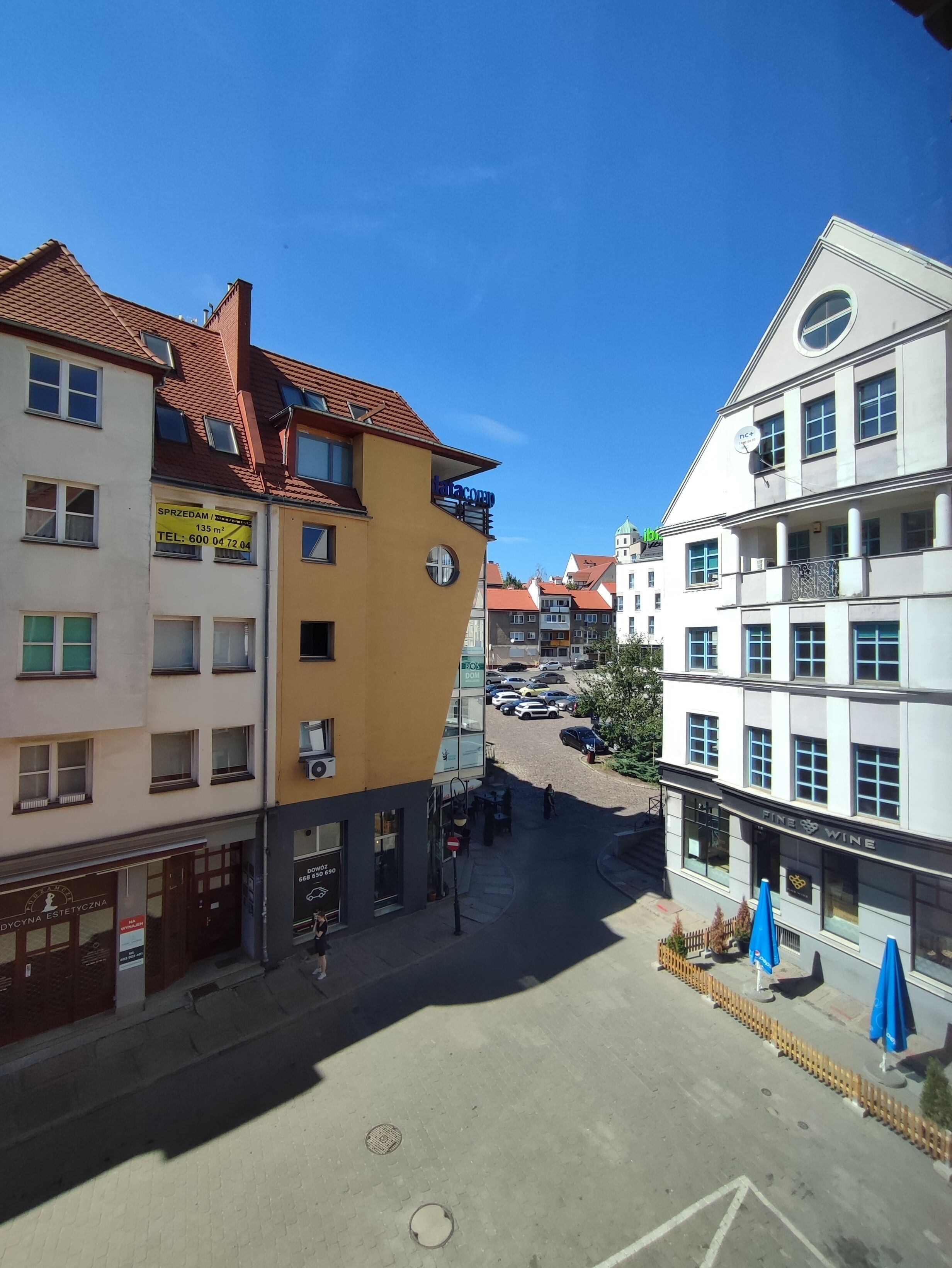 A street view with buildings, including a yellow building with a sign, a white building with a sign, and a blue awning.