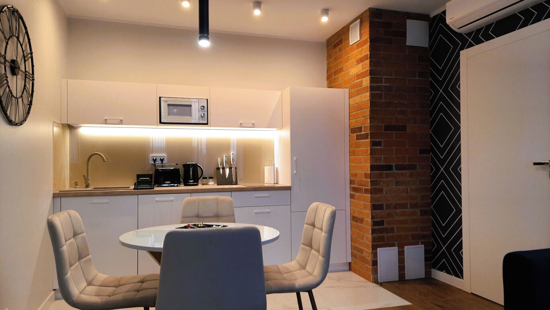 A modern kitchen with a round dining table and four chairs, a microwave, and a coffee maker.