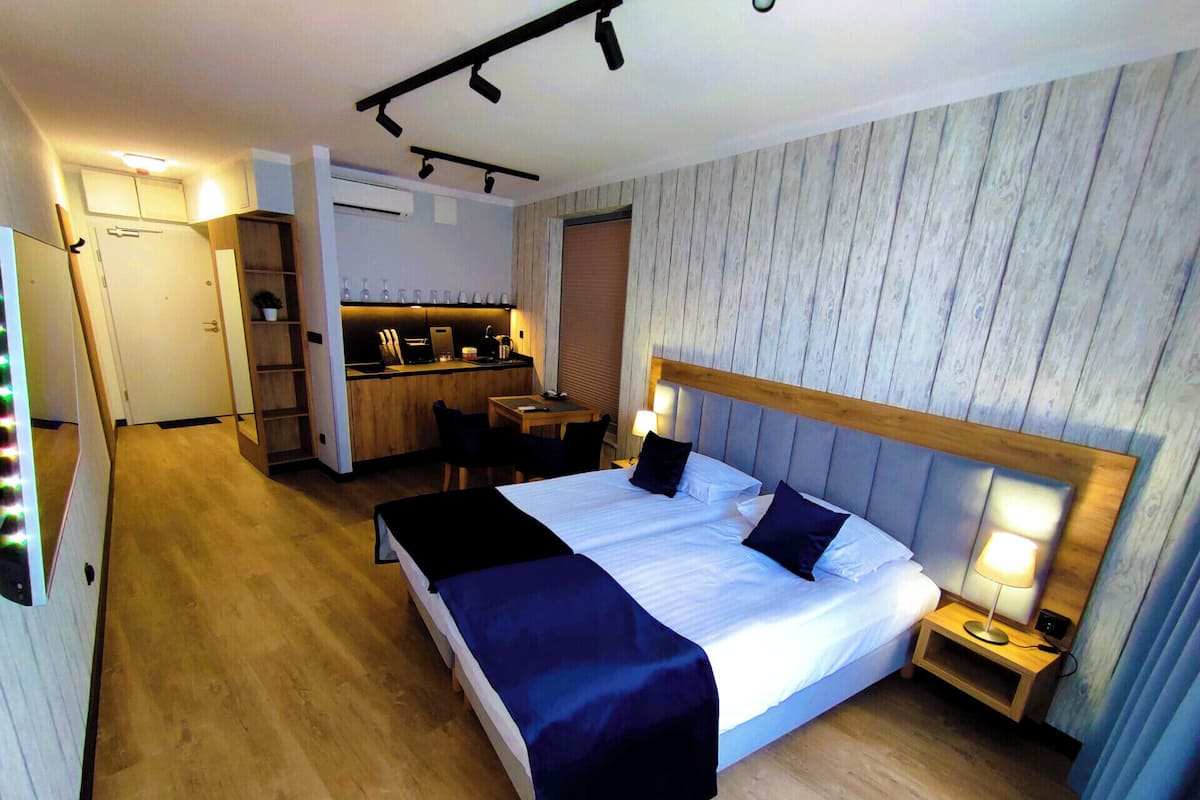 A hotel room with a bed, bedside table, and a kitchenette area.