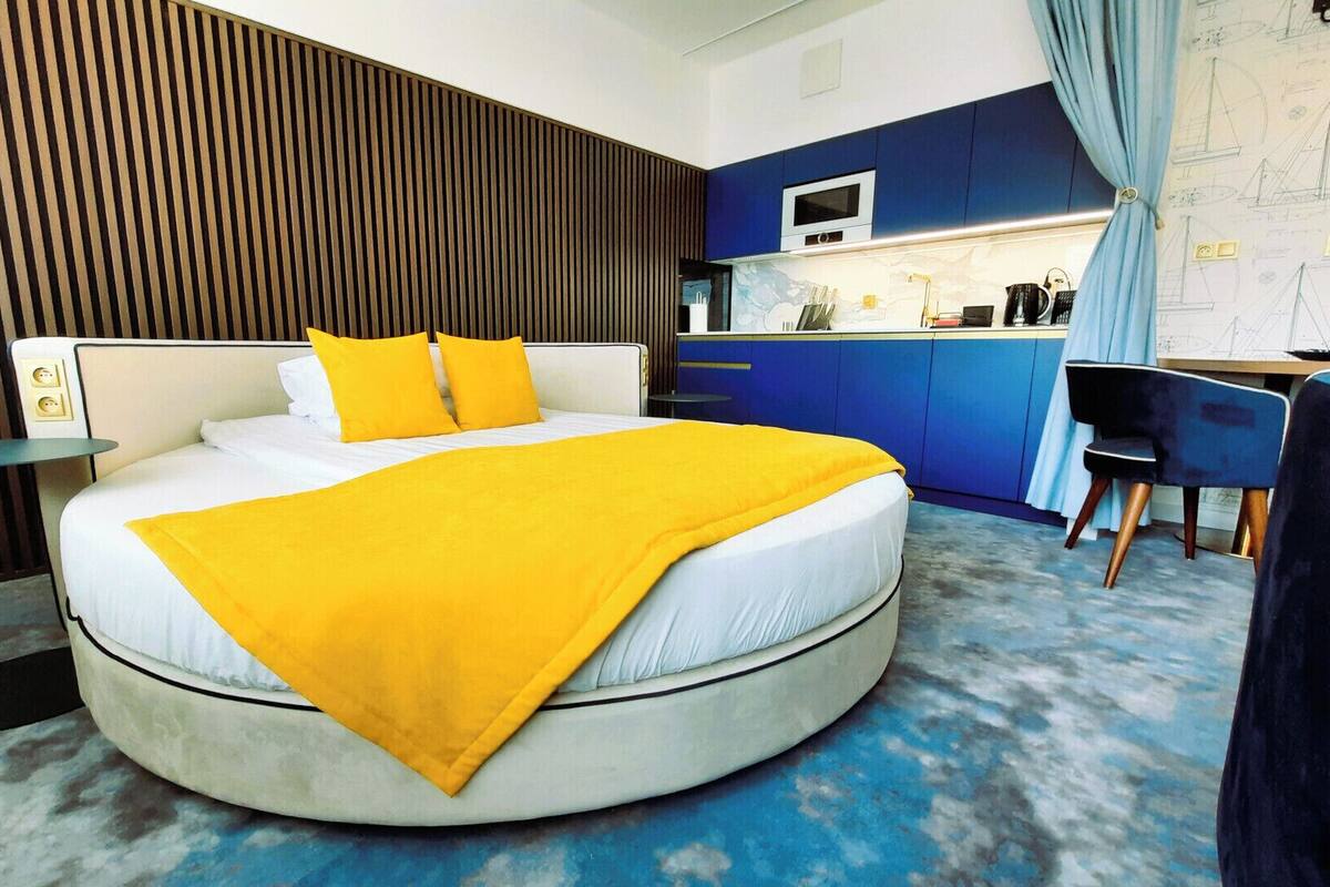 A modern hotel room with a round bed, a kitchen area, and a dining table.