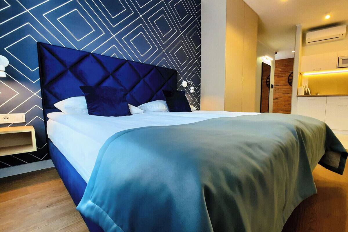 A modern hotel room with a large bed, a desk, and a kitchenette.