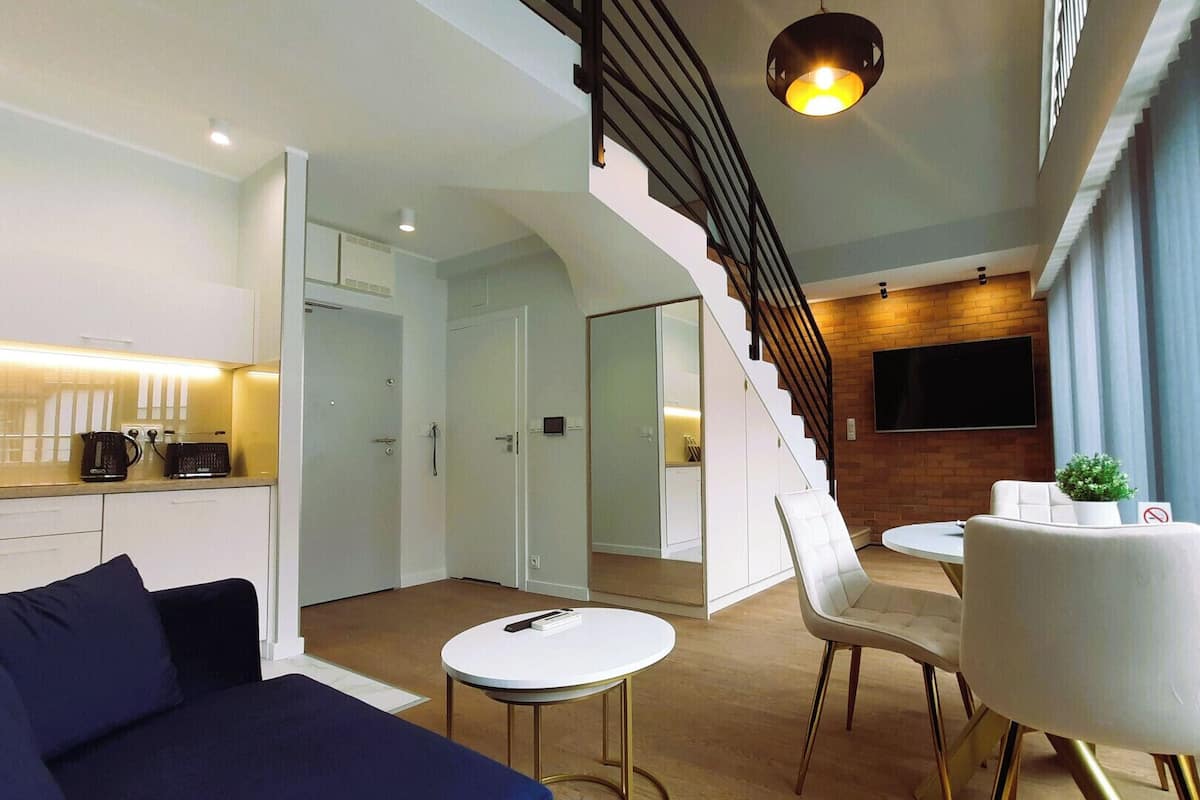 A modern living room with a staircase, a dining area, and a kitchen.