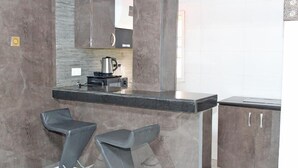 A modern kitchen with a marble countertop, two bar stools, and a coffee machine. - The Regal Boutique Hotel (Abuja)