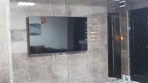 A modern room with a large flat-screen TV mounted on a textured wall, a marble floor, and a black door with a diamond-patterned window. - The Regal Boutique Hotel (Abuja)