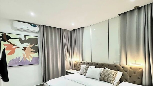 A modern bedroom with a large bed, a bedside table, an air conditioning unit, a wall-mounted artwork, and a wardrobe. - The Regal Boutique Hotel (Abuja)