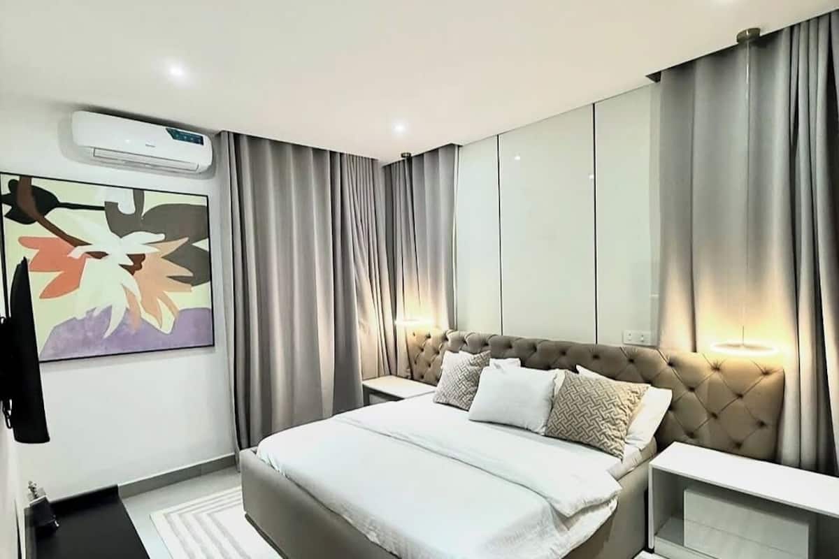 Une chambre moderne avec un grand lit, une table de chevet, un appareil de climatisation, une œuvre d’art accrochée au mur et une armoire.