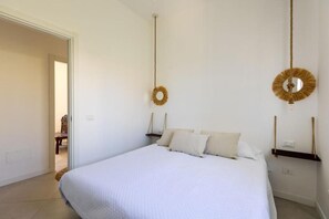 A bedroom with a large bed, a door leading to another room, and a wall-mounted circular mirror. - Villa Bianca (Avola)