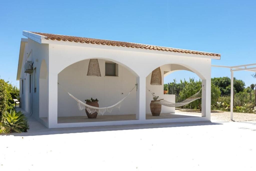 A white building with a tiled roof, two arched windows, and a covered porch with two hammocks.