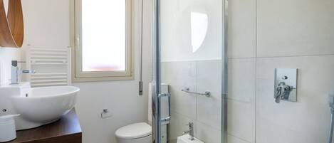 Ein modernes Badezimmer mit einer Duschkabine, einem weißen Waschbecken und einer Toilette.
